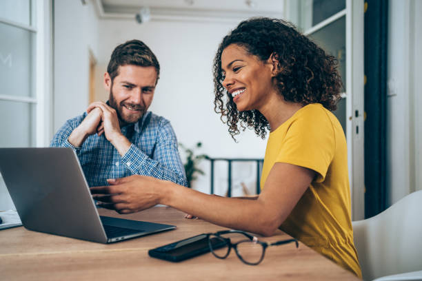Shot of two successful businesspeople working together on a laptop in modern office. Businessman and businesswoman in meeting using laptop and discussing business strategy. Two business people talking in the office.
